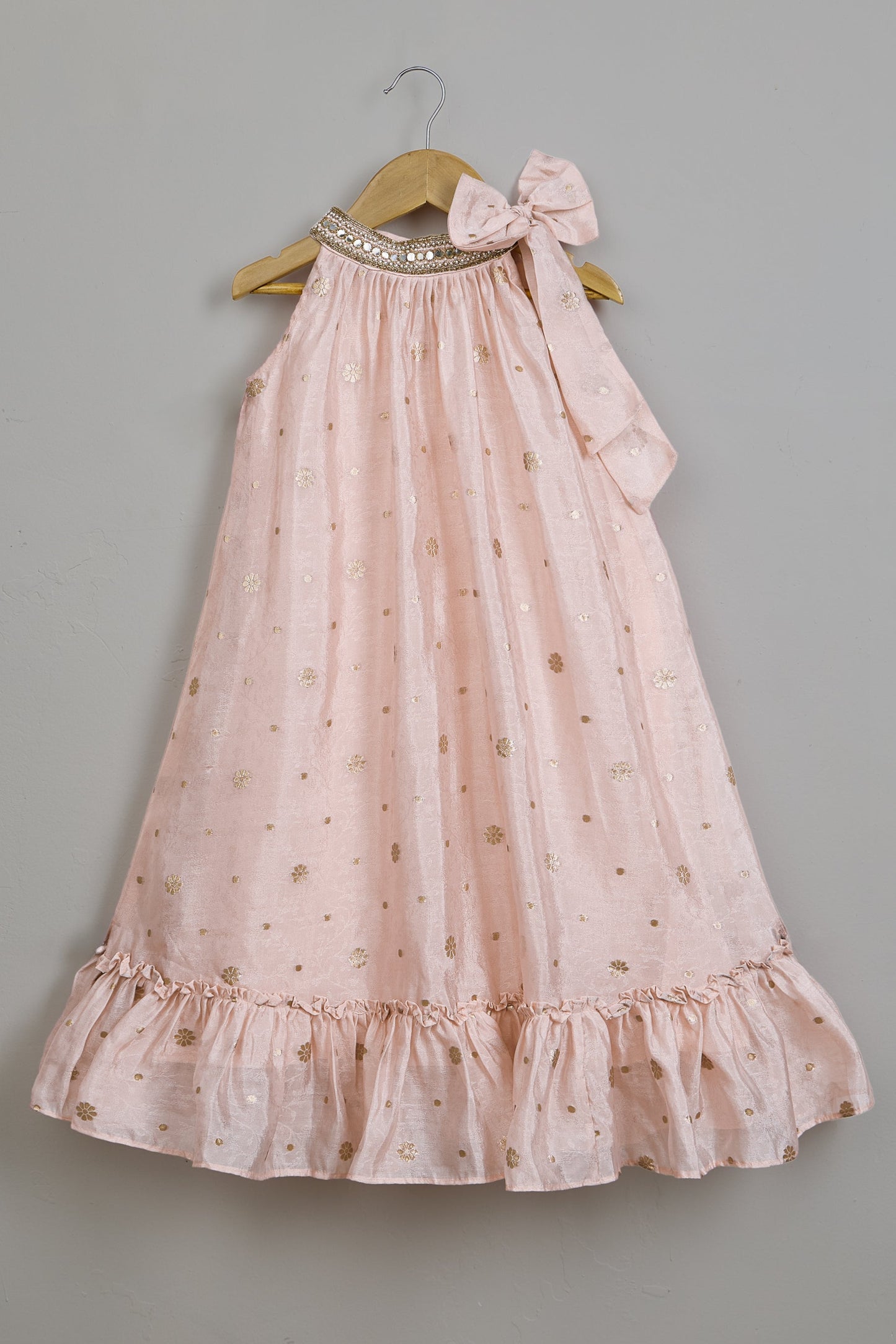 Pink dress with ruffles and a bow on a hanger against a gray background.