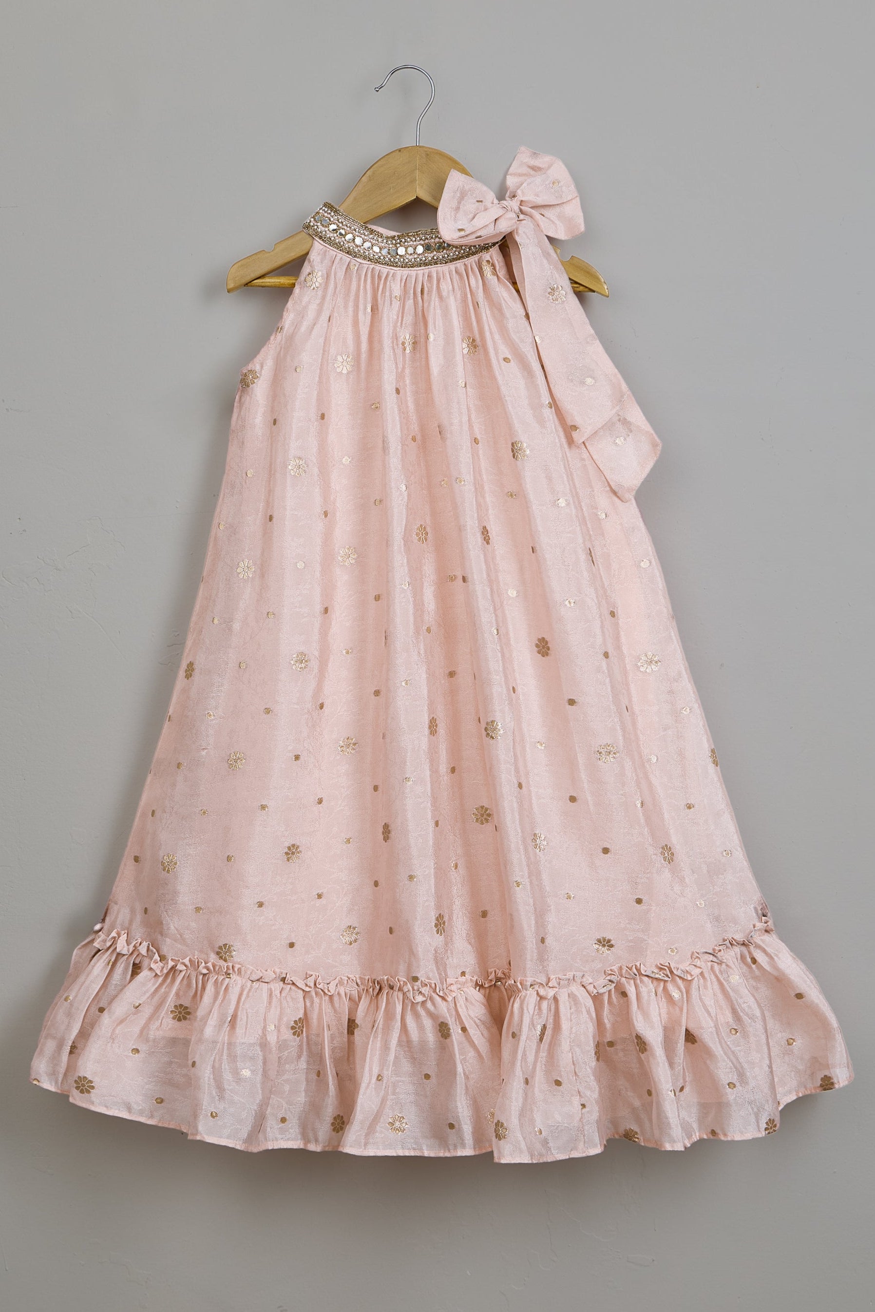 Pink dress with ruffles and a bow on a hanger against a gray background.