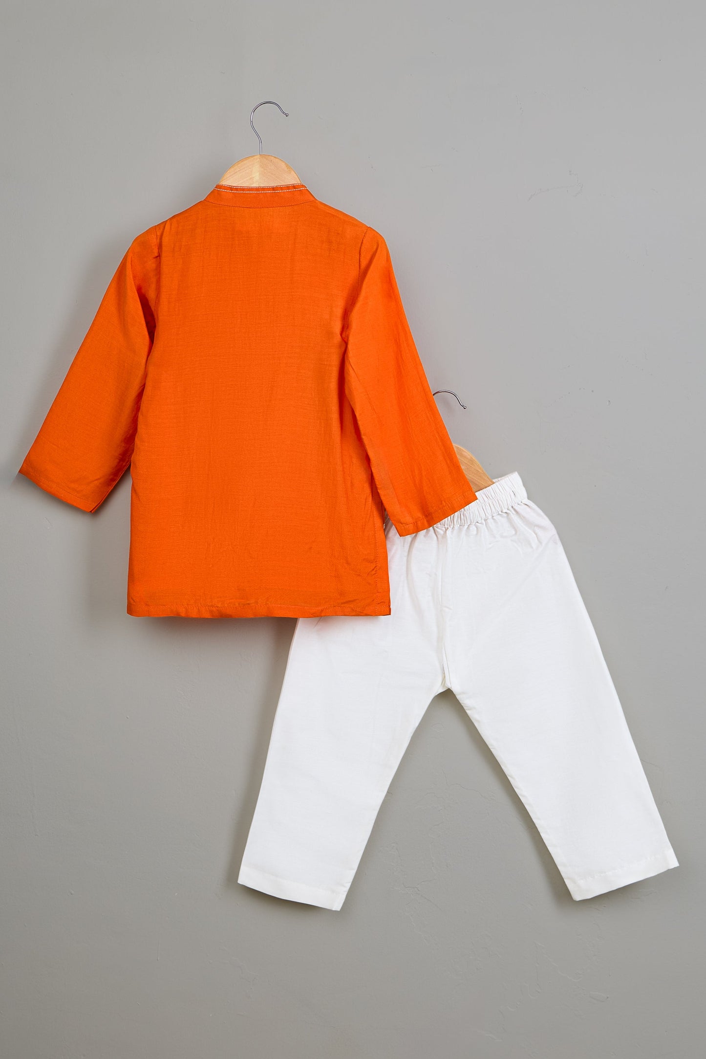 Orange Kurta and white pants on hangers against a gray background