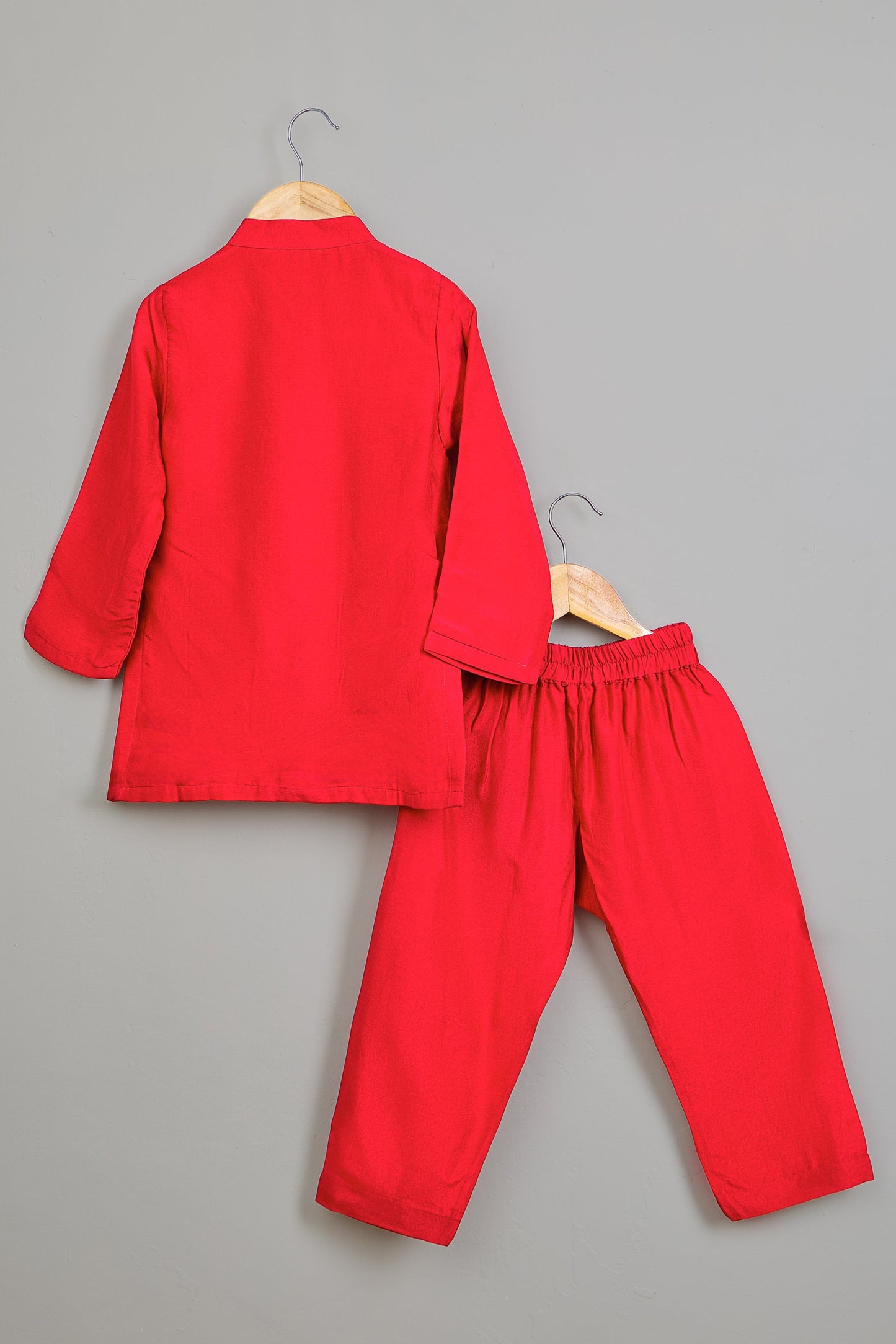 Red outfit with a top and pants on hangers against a gray background
